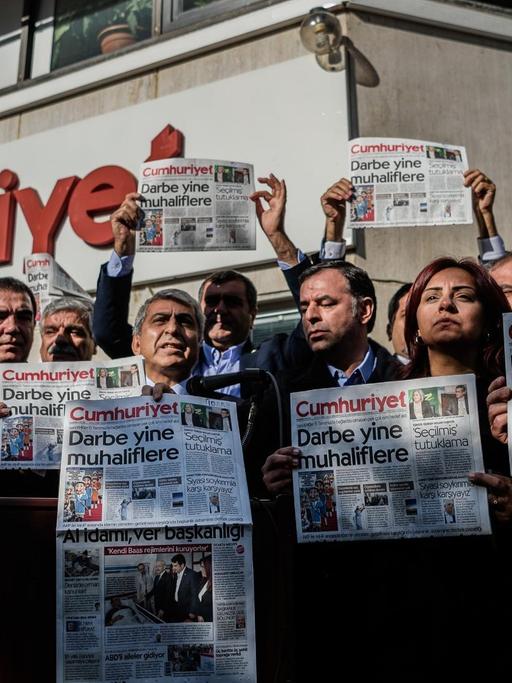 Männer und Frauen stehen vor dem "Cumhuriyet"-Gebäude und halten Ausgaben der Zeitung mit der Aufschrift "Putsch gegen die Opposition" in die Höhe.