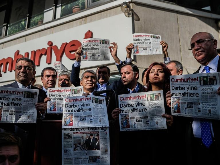 Männer und Frauen stehen vor dem "Cumhuriyet"-Gebäude und halten Ausgaben der Zeitung mit der Aufschrift "Putsch gegen die Opposition" in die Höhe.