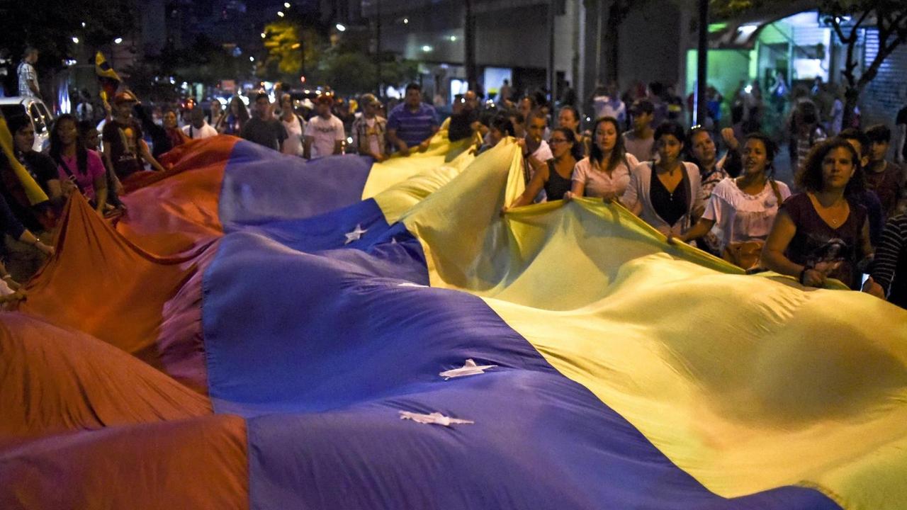 Man sieht viele Menschen und eine riesige Fahne von Venezuela in rot-blau-gelb.