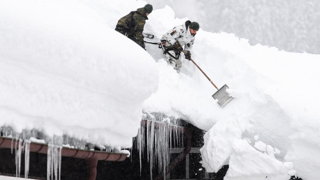  Einsatzkräfte der Bundeswehr stehen auf einem Dach im bayerischen Buchenhöhe das Dach und schippen die Schneemassen weg.