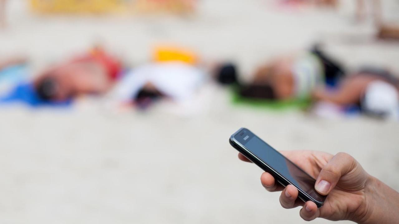 Eine Frau schreibt am 04.08.2013 mit einem Mobiltelefon eine SMS am Strand von Kolberg, Polen, an der Ostsee.