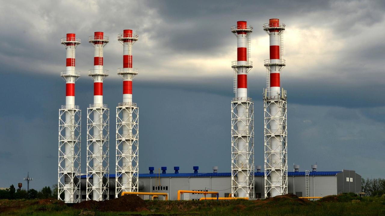 Rot-weiß gestrichene Türme eines Gaskraftwerks vor dunklem Wolkenhimmel.