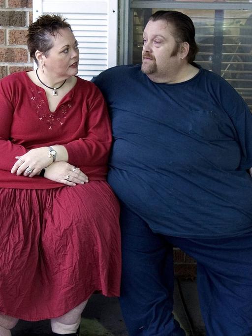 Ein stark übergewichtiges Paar sitzt auf einer Bank vor ihrem Haus.