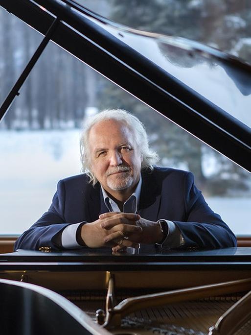 Der Dirigent Donald Runnicles sitzt hinter seinem Piano vor einem Fenster, durch das eine winterliche Landschaft zu sehen ist.
