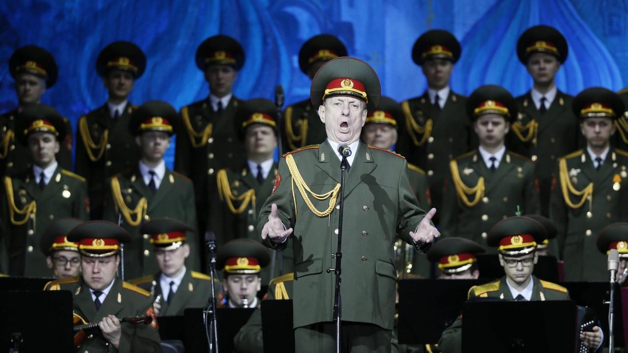 Der Solist Wladislaw Golikow singt während eines Konzertes. Im Hintergrund ist der Alexandrow-Chor in Militäruniformen zu sehen.