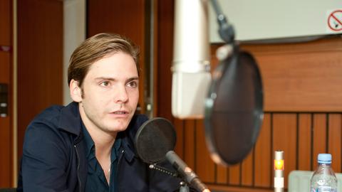 Der Schauspieler Daniel Brühl sitzend im Studio am Mikrofon.