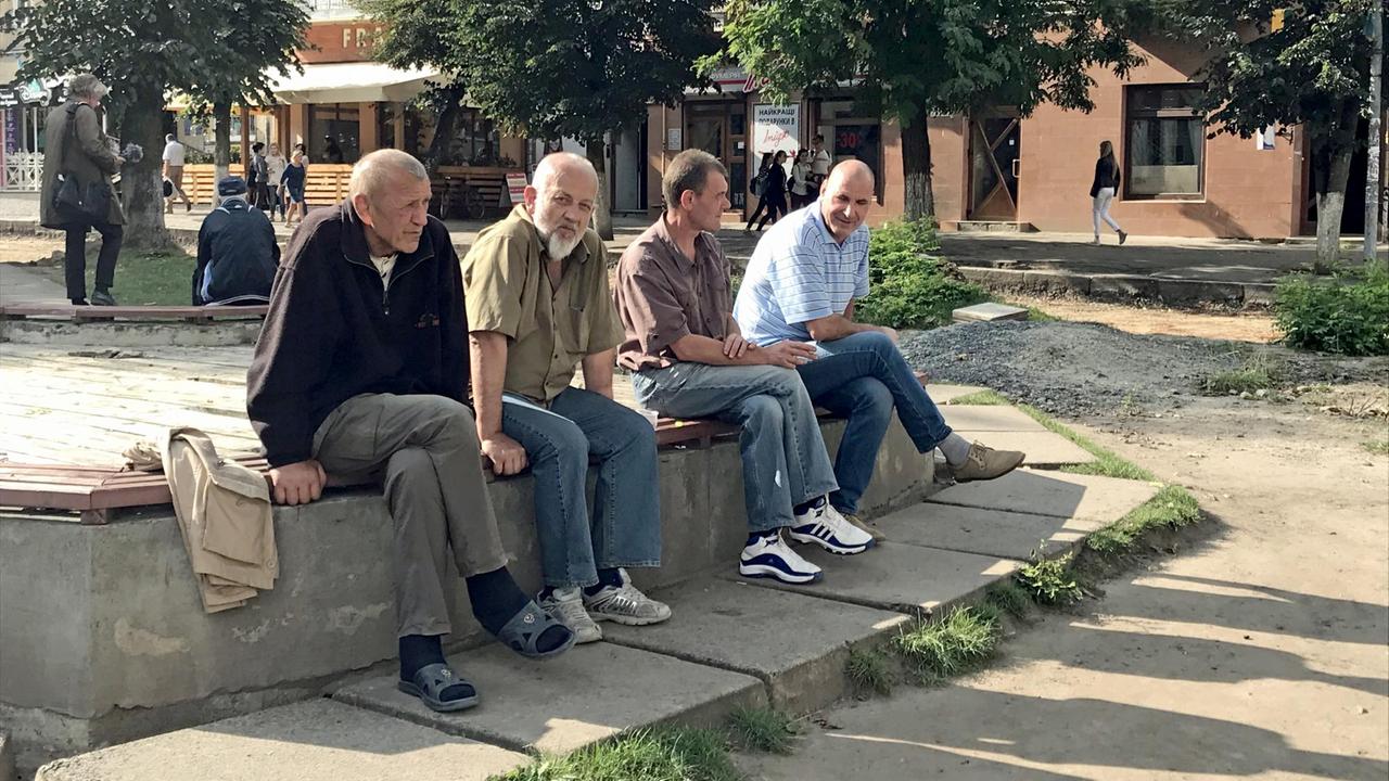Alte Männer sitzen in der urkainischen Stadt Drohobytsch auf einer kleinen Mauer.