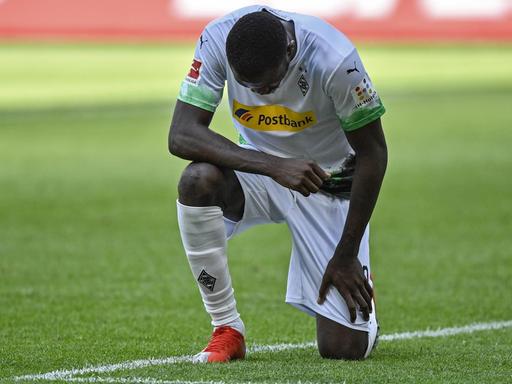 Das Foto zeigt den Fußballer Marcus Thuram von Borussia Mönchengladbach. Er kniet nach einem Treffer und setzt damit ein Zeichen gegen Rassismus.