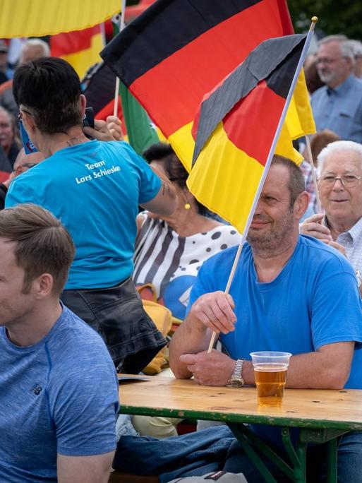 Beim AfD-Wahlkampfauftakt in Brandenburg sitzen Teilnehmer teilweise mit Deutschlandfahnen auf Bierbänken und warten auf die Redner.