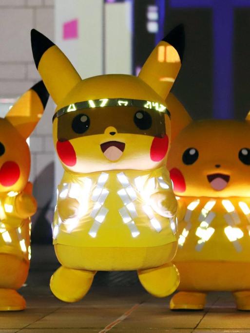 Fünf menschengroße Pikachus (ein gelbes. hasenähnliches Wesen mit langen Ohren, die an der Spitze schwarz sind) mit LED-Lichtern tanzen auf einer Bühne.