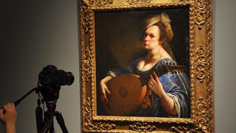 Artemisia Gentileschis Gemälde "Selbstporträt als Lautenspielerin". Eine Frau des Barock spielt eine Laute und schaut in Richtung des Betrachters.