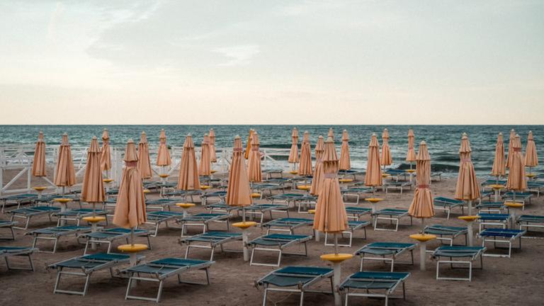 Leere Sonnen-Liegen stehen an einem Strand.