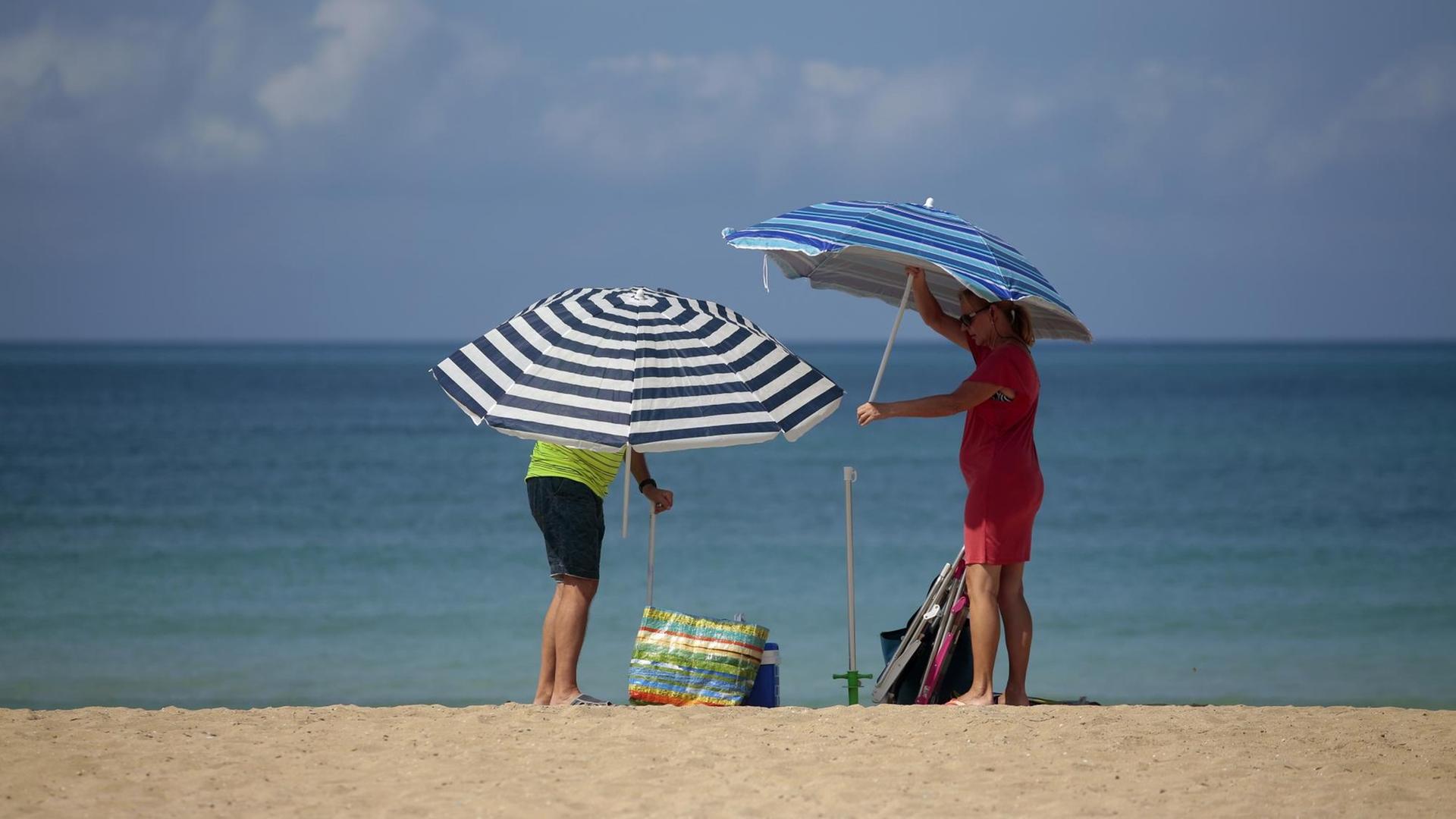 Ein Paar stellt am Strand 2 Sonnen-Schirme auf.