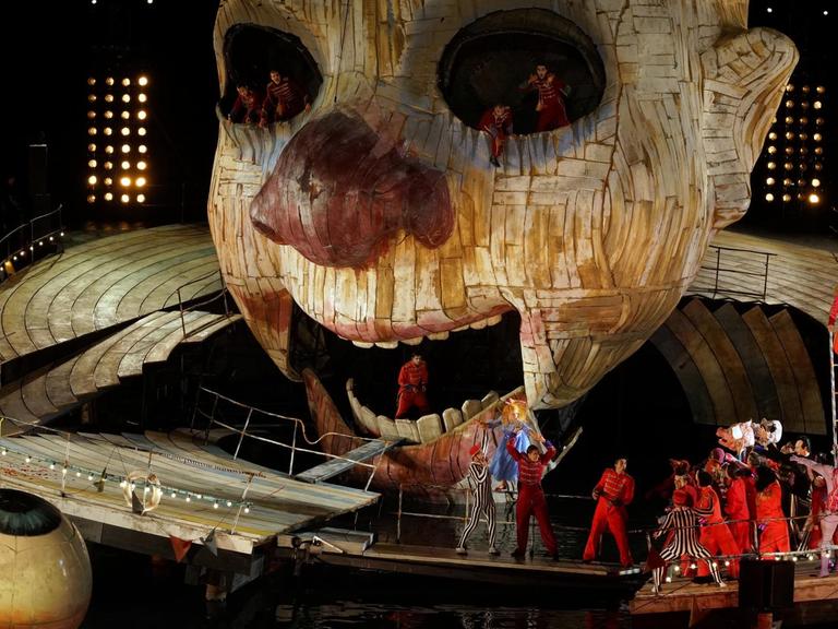 Das Foto zeigt das Bühnenbild aus "Rigoletto", inszeniert von Philipp Stölzl auf der Seebühne Bregenz: Ein riesiger Holzkopf, um den sich die Sänger gruppieren.