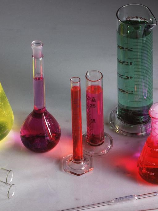 Laborgefäße, wie Glaskolben und Messzylinder, mit verschiedenfarbigen Flüssigkeiten