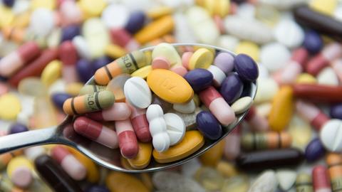 Zahlreiche Pillen und Tabletten liegen auf einem Tisch und auf einem Löffel.