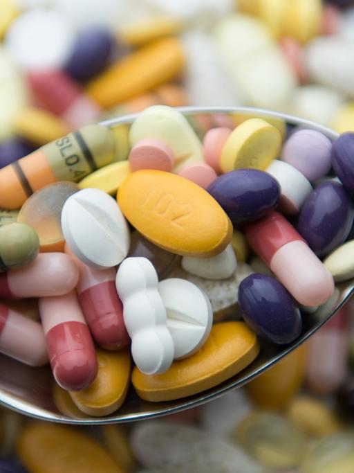 Zahlreiche Pillen und Tabletten liegen auf einem Tisch und auf einem Löffel.