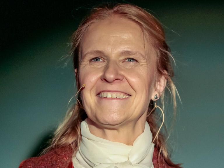 Cornelia Funke vor grünlichem Hintergrund, bei einer Lesung.