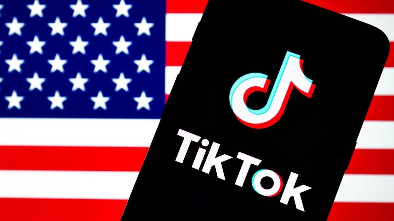 Auf dem Bild ist ein Smartphone mit dem TikTok-Logo vor einer US-Flagge zu sehen