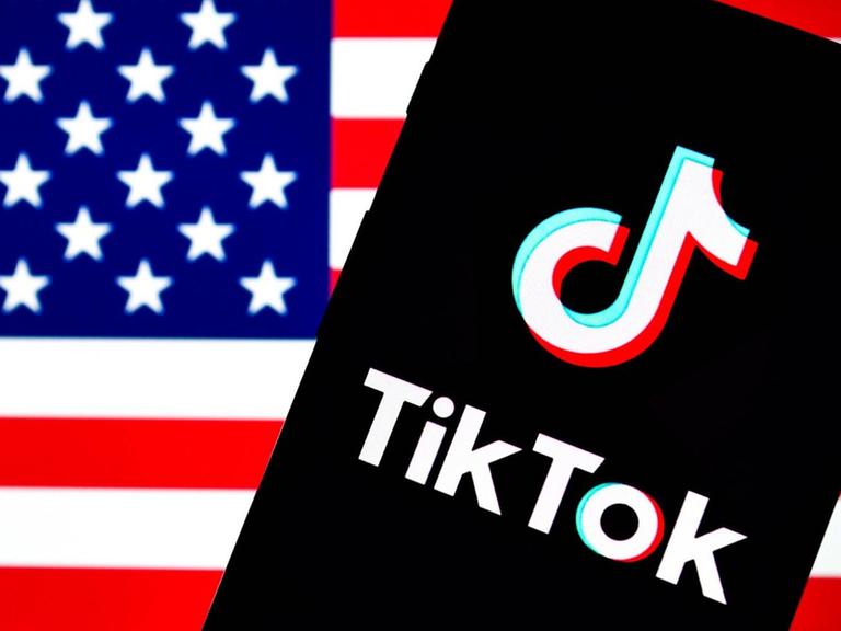 Auf dem Bild ist ein Smartphone mit dem TikTok-Logo vor einer US-Flagge zu sehen