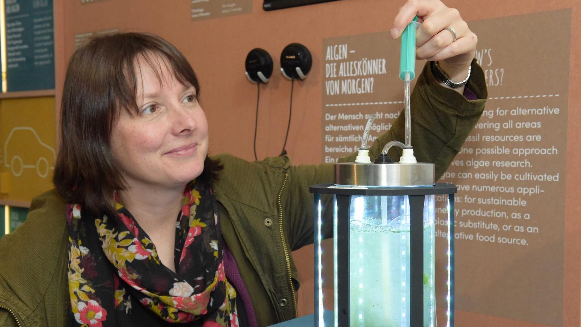 Eine Frau bedient einen kleinen Reaktor, der Mikroalgen produziert. Zu sehen ist er in der Ausstellung "Zukunft gestalten - Wie wollen wir leben?"