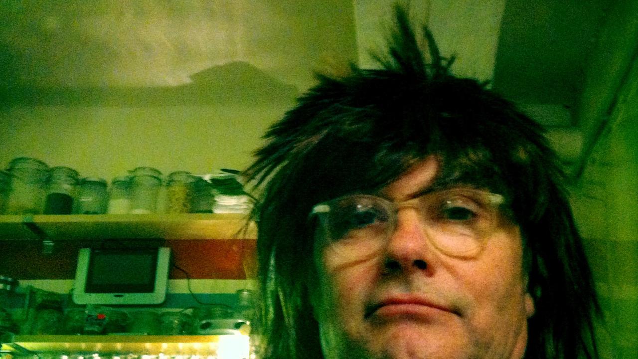 Zu sehen ist der Kabarettist, Liedermacher, Buchautor und Komponist Thomas Pigor in seiner Küche vor dem Gewürzregal. Er trägt eine schwarze Perücke mit abstehenden Haaren.