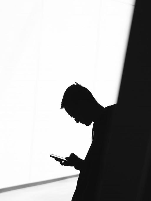 Silhouette eines Mannes der auf seinem Telefon eine Nummer wählt.