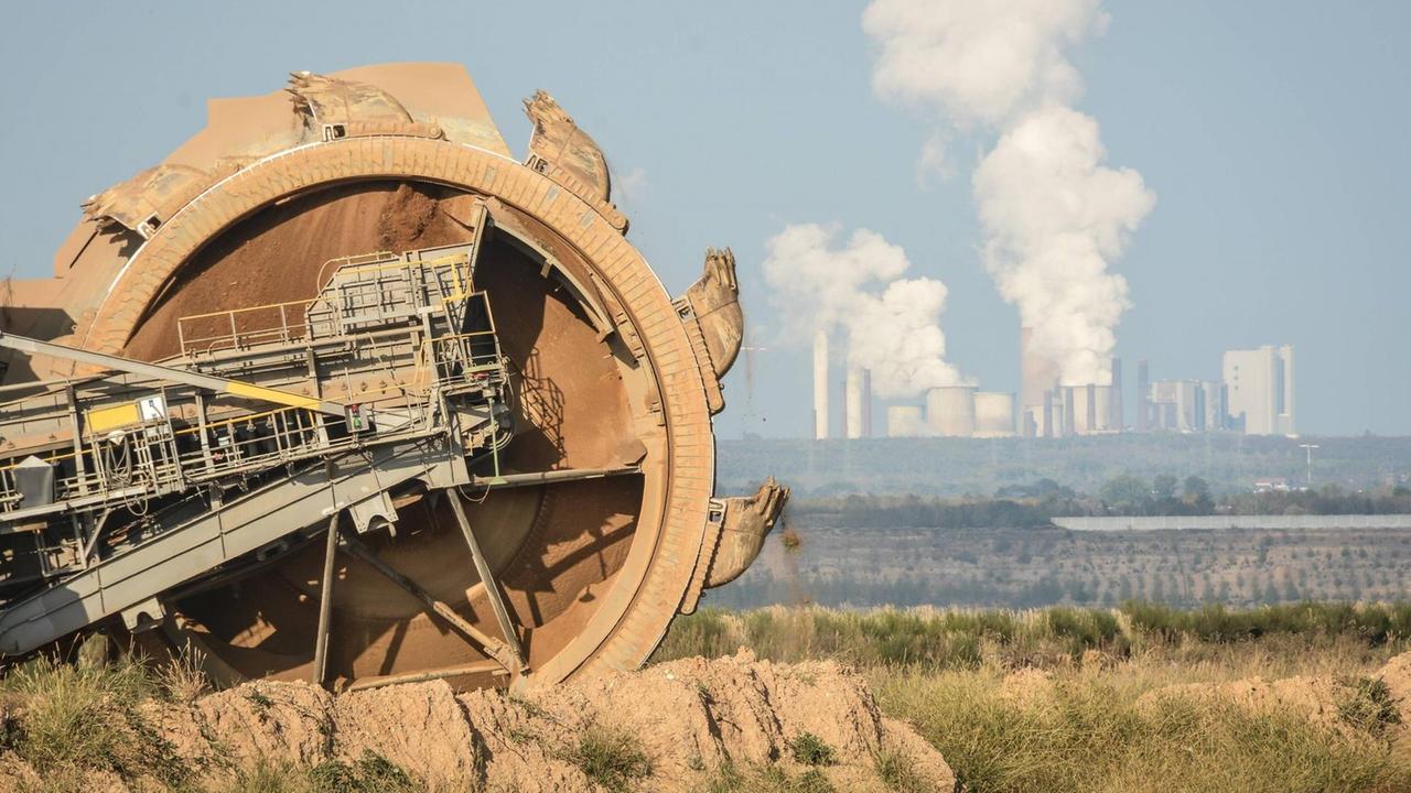 Ein Schaufelradbagger von RWE hinter dem Hambacher Forst vor dem Tagebau Etzweiler. Im Hintergrund das RWE Kraftwerk Niederaußem.