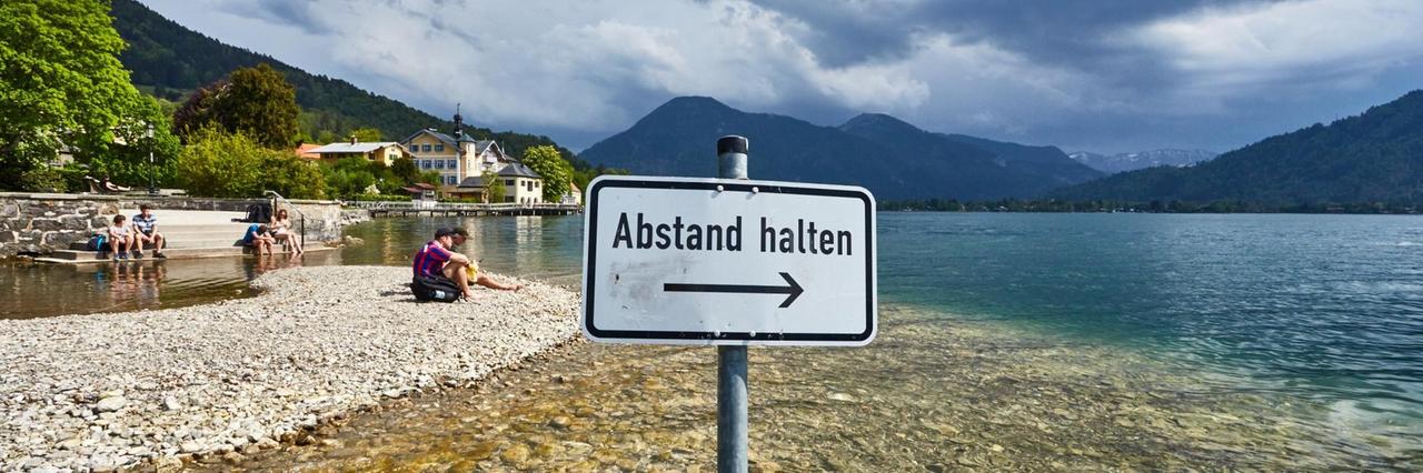 Ein Schild mit der Aufschrift "Abstand halten" an einem idyllischen See.