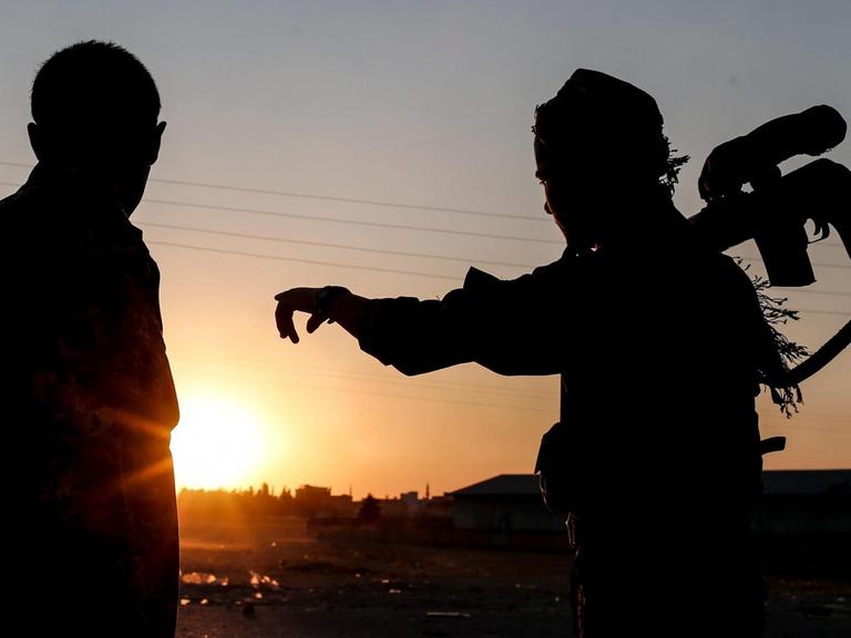 Zwei Mitglieder der kurdischen YPG-Truppen blicken auf den Sonnenuntergang beim Grenzübergang Tel Abyad in Nord-Syrien.