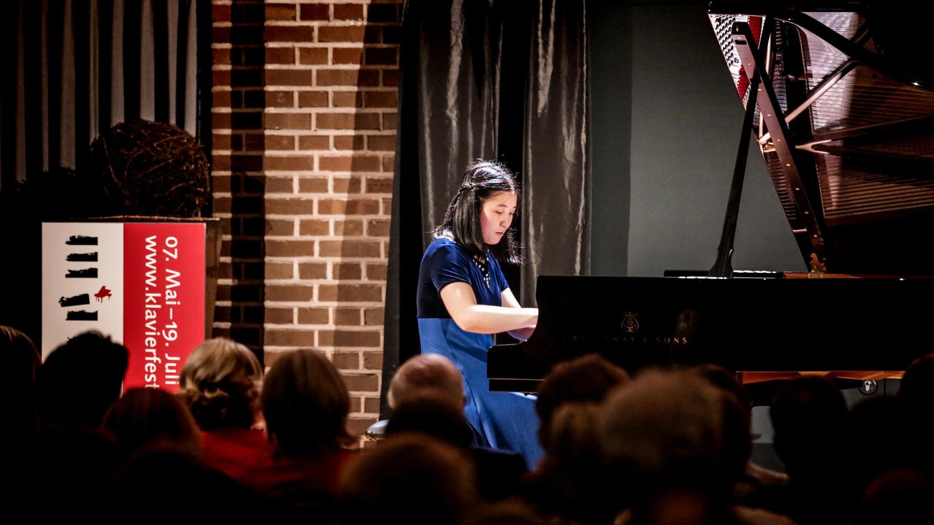 Eine Pianistin im blauen Kleid sitzt an einem Flügel. Sie blickt konzentriert auf die Tasten. Es ist Lauren Zhang. Sie spielte am 9. Mai 2019 in Bochum, in der Alten Lohnhalle.