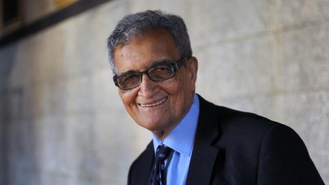 Amartya Sen steht vor einer Mauer und schaut freundlich in die Kamera.