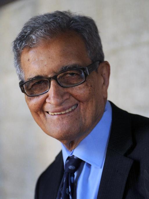 Amartya Sen steht vor einer Mauer und schaut freundlich in die Kamera.