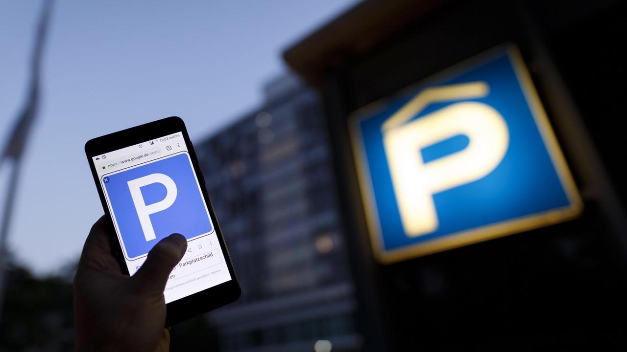 Ein beleuchtetes Parkhausschild und eine Hand, die ein Handy hält 