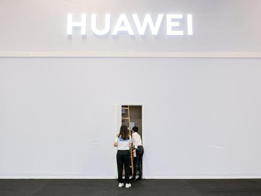 Zwei Mitarbeiter des Technologieunternehmen Huawei in der Internationalen Funkausstellung (IFA) stehen vor einem Seiteneingang des Standes.