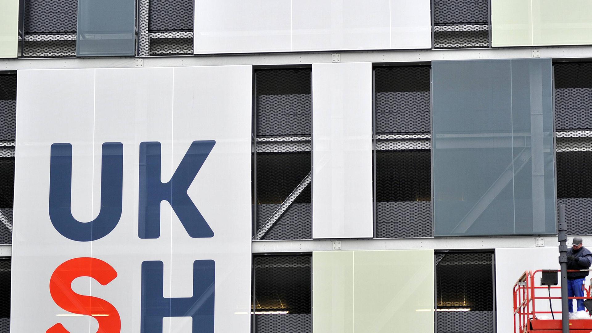 Fassade des Universitätsklinikums in Kiel mit den Buchstaben UKSH, rechts im Bild ein Bauarbeiter auf einem Kran.