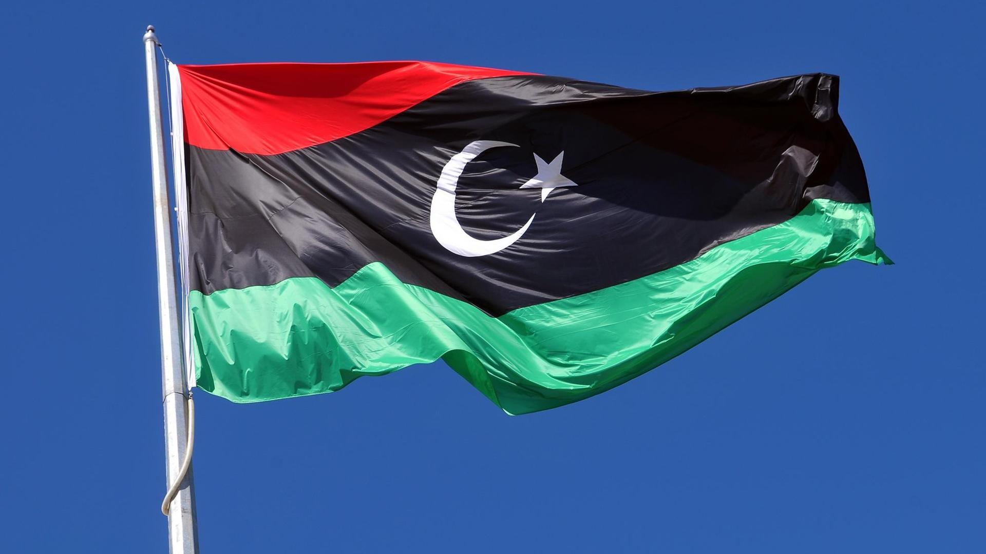 Die libysche Flagge weht im Wind vor blauem Himmel.