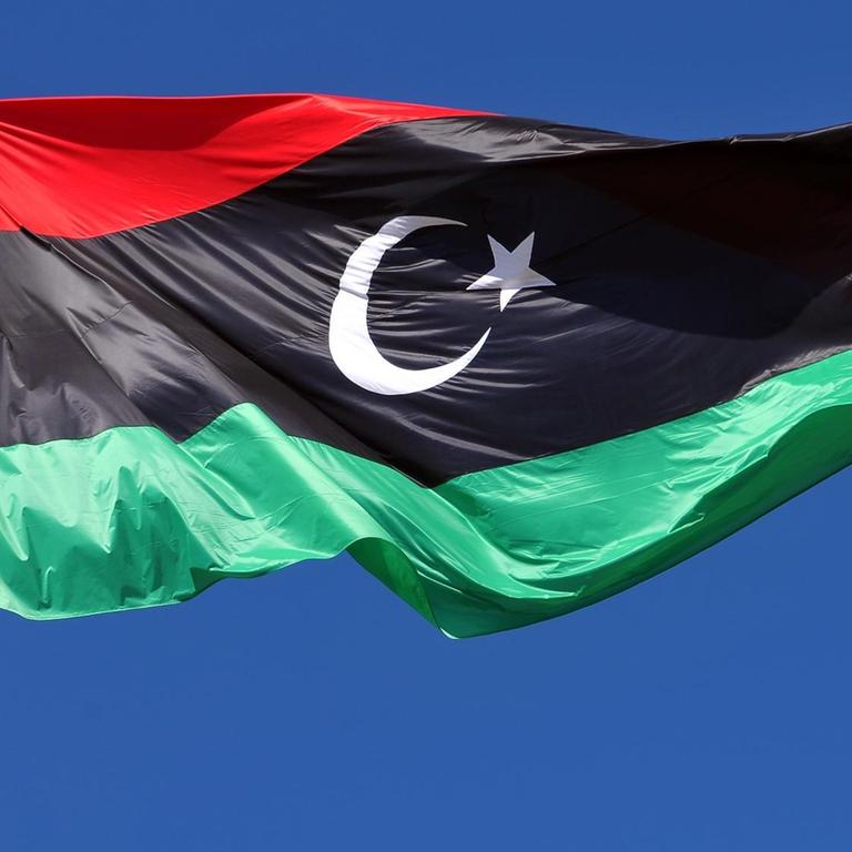 Die libysche Flagge weht im Wind vor blauem Himmel.