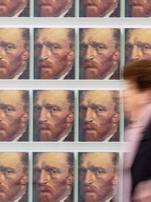 Eine Besucherin geht in der Ausstellung "Making van Gogh" an Katalogen mit einem Selbstporträt des Malers vorbei.