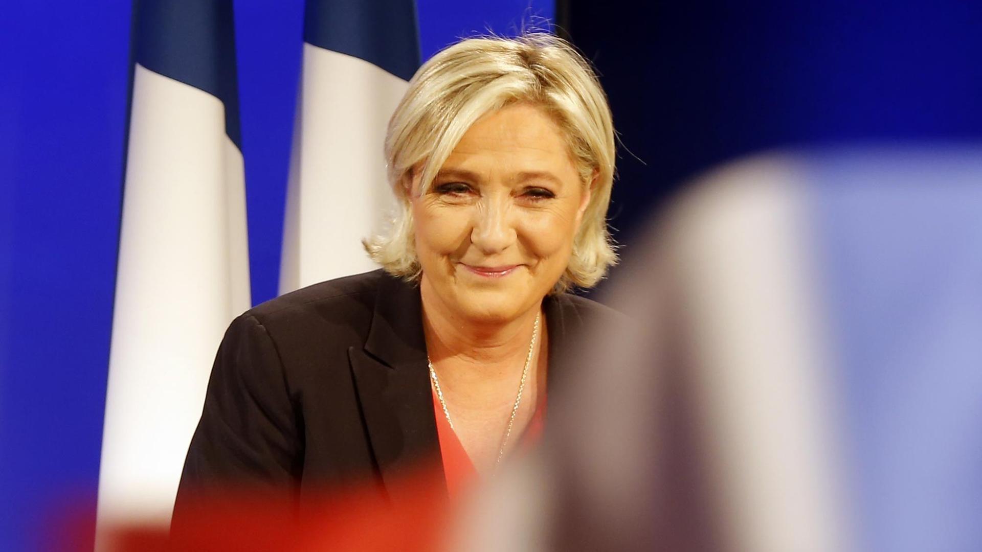 Parteichefin Marine Le Pen hält im Wahl-Hauptquartier des Front National eine Rede - französische Flaggen im Hintergrund.