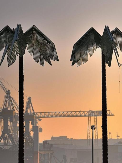 Zwei künstliche Palmen stehen im rötlichen Abendlicht am Hamburger Hafen.