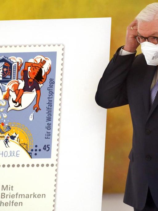 Bundespräsident Frank-Walter Steinmeier nimmt im Schloss Bellevue seine Mund-Nasenschutzmaske ab, bevor der Bundesfinanzminister ihm die Wohlfahrtsmarken 2021 übergibt.