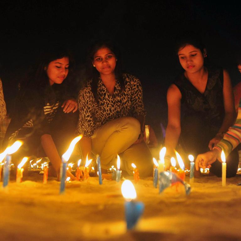 Feierlichkeiten zum indischen Diwali Festival: junge Menschen zünden auf dem Boden stehende Kerzen an