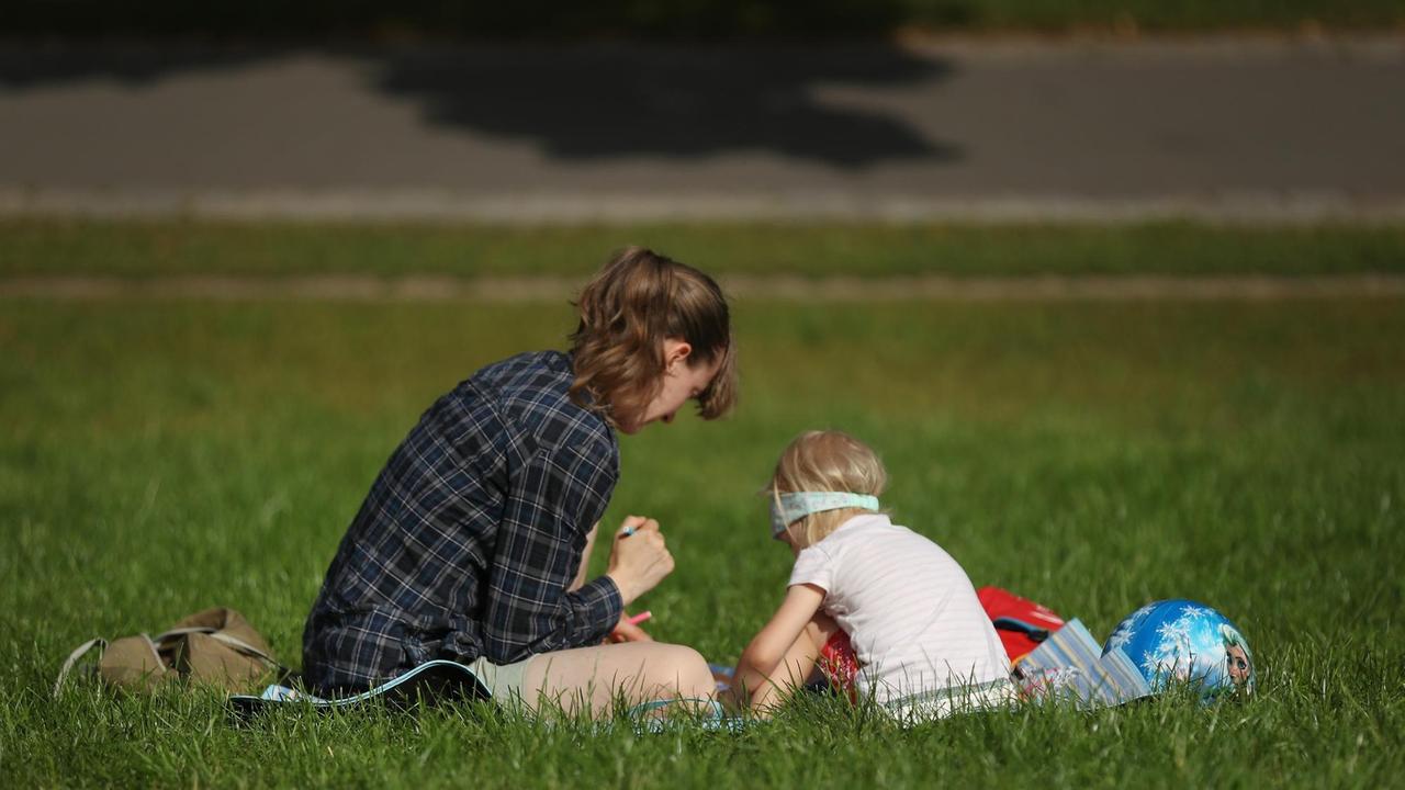 Eine Mutter sitzt mit ihrem Kind auf einer Wiese in einem Berliner Park
