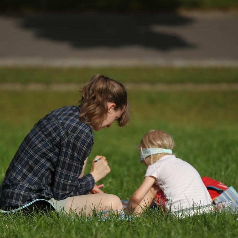 Eine Mutter sitzt mit ihrem Kind auf einer Wiese in einem Berliner Park
