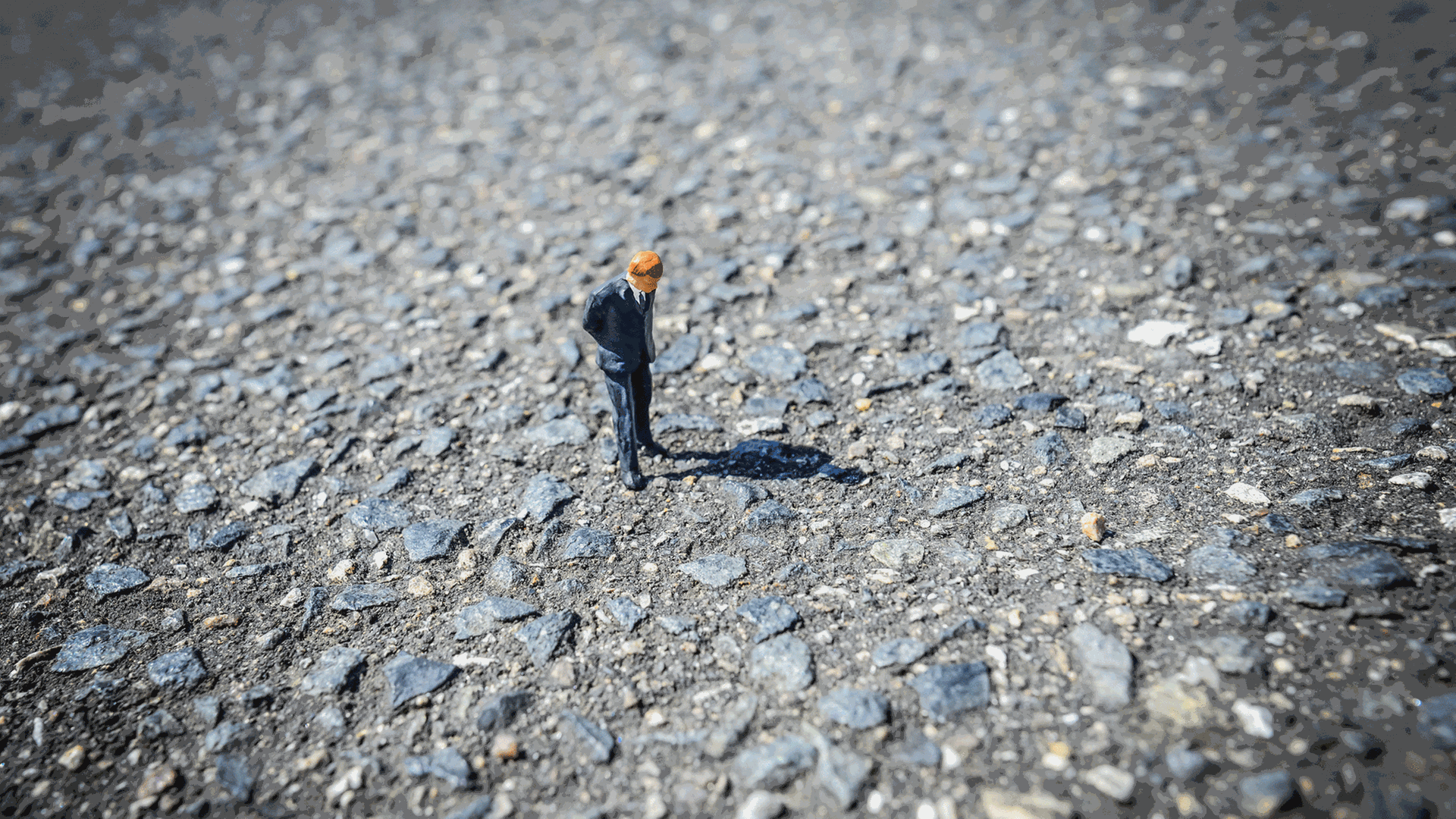 Eine Miniaturfigur steht auf einer steinigen Straße und schaut auf den Boden.