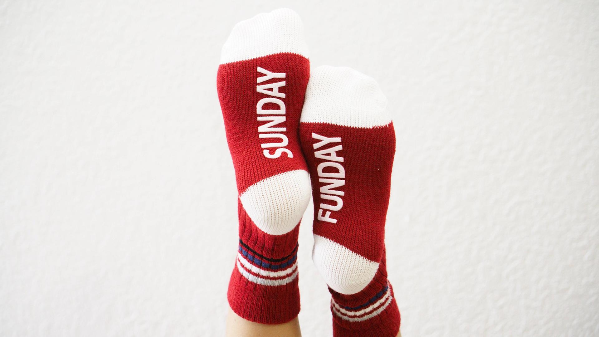 Zwei hochgelegte Füße mit roten Socken und dem Aufdruck "Sonntag"