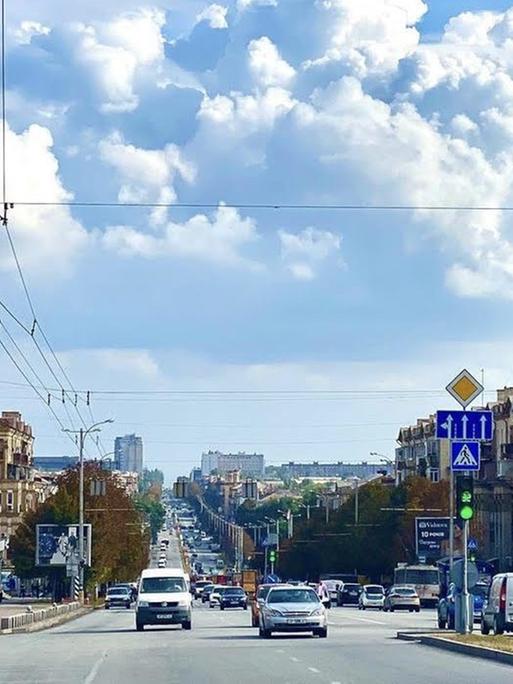 In der Innenstadt von Saporischschja warten Autos an einer Ampelkreuzung. Links ist eine Oberleitung für eine Straßenbahn. Wolken sind am Himmel.