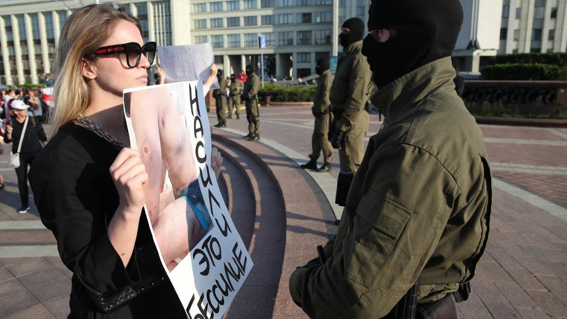 Eine mutige junge Frau steht vor einem Polizisten während der Proteste in Minsk gegen den Präsidenten Lukaschenko. Sie konfrontiert ihn mit einem Plakat, auf dem Wunden eines von der Polizei malträtierten Demonstranten zu sehen sind. Auf dem Plakat steht auf belarussisch: Gewalt ist Schwäche.