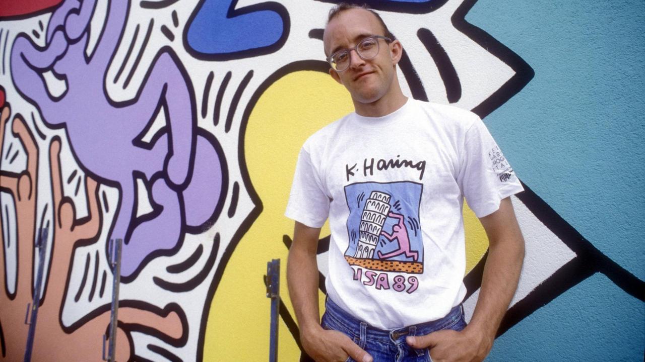 Das Bild zeigt Keith Haring im Jahr 1989 vor einer seiner Wandmalereien in Pisa.  